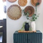 shows a black and white vintage looking vases siting on a wood plank and teal cabinet with greenery hanging out of them with a wicker basket wall in the background