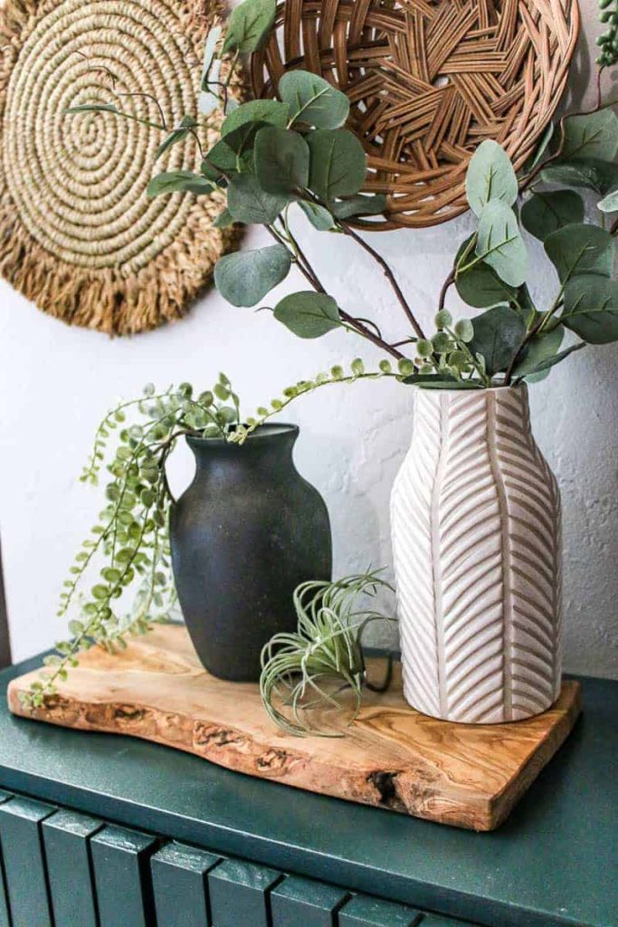 A black painted upcycled vase sits next to a different white ceramic vase, both filled with eucalyptus leaves.