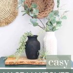 shows a black and white vintage looking vases siting on a wood plank and teal cabinet with greenery hanging out of them with a wicker basket wall in the background with overlay text that says easy vase makeover (spray paint and dirt)