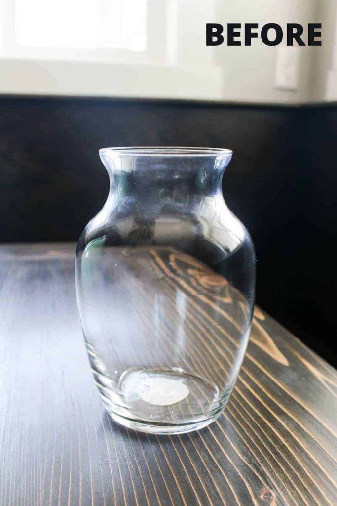 A clear glass vase sits on a wood table. Learn how to upcycle this dollar store vase into gorgeous DIY vintage pottery.