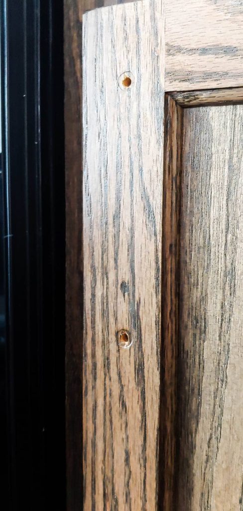 A close up picture of a stained wood cabinet door with a repaired nail hole using Mohawk wood repair products.