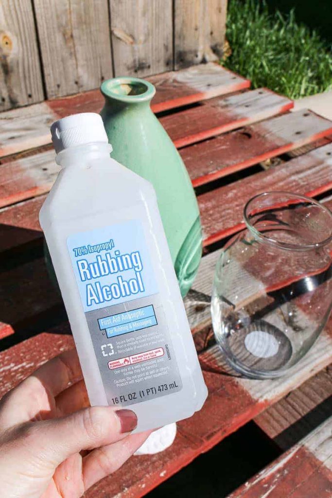 A green and clear glass vase in the background, and a bottle of rubbing alcohol in the foreground.