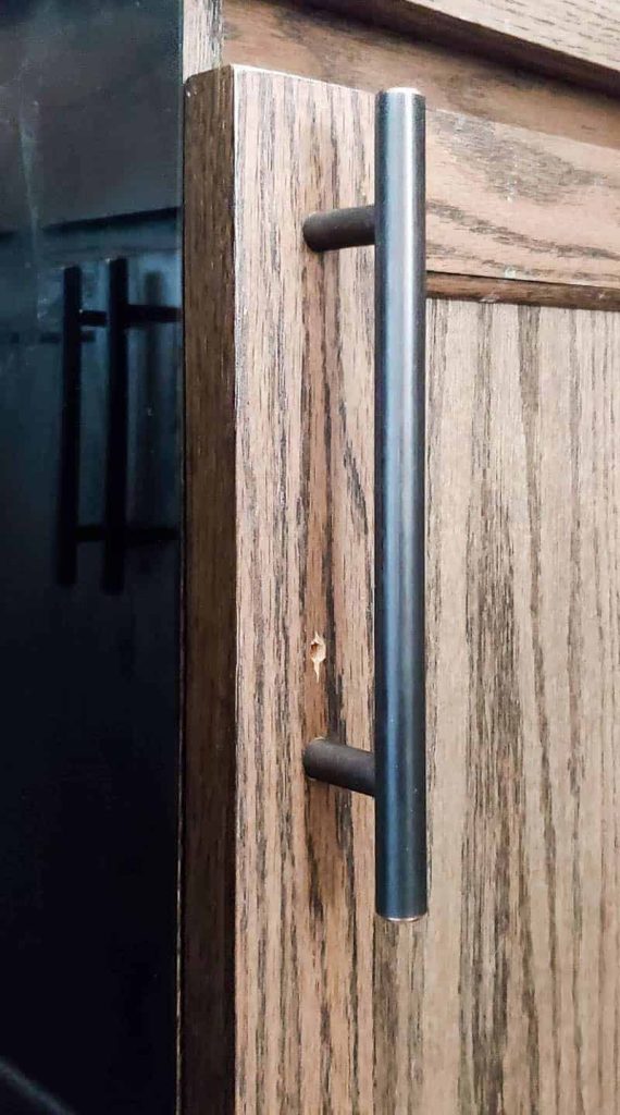 A close up look at a nail hole in a stained wood cabinet door. We learned how to repair nail holes on stained wood to hide this hole on the cabinet door.