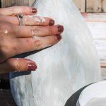 shows a hand touching a vase covered in joint compound outside on a wood pallet