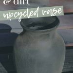 shows a black glass vase sitting on a wood pallet outside with overlay text that says spray paint and dirt upcycle vase