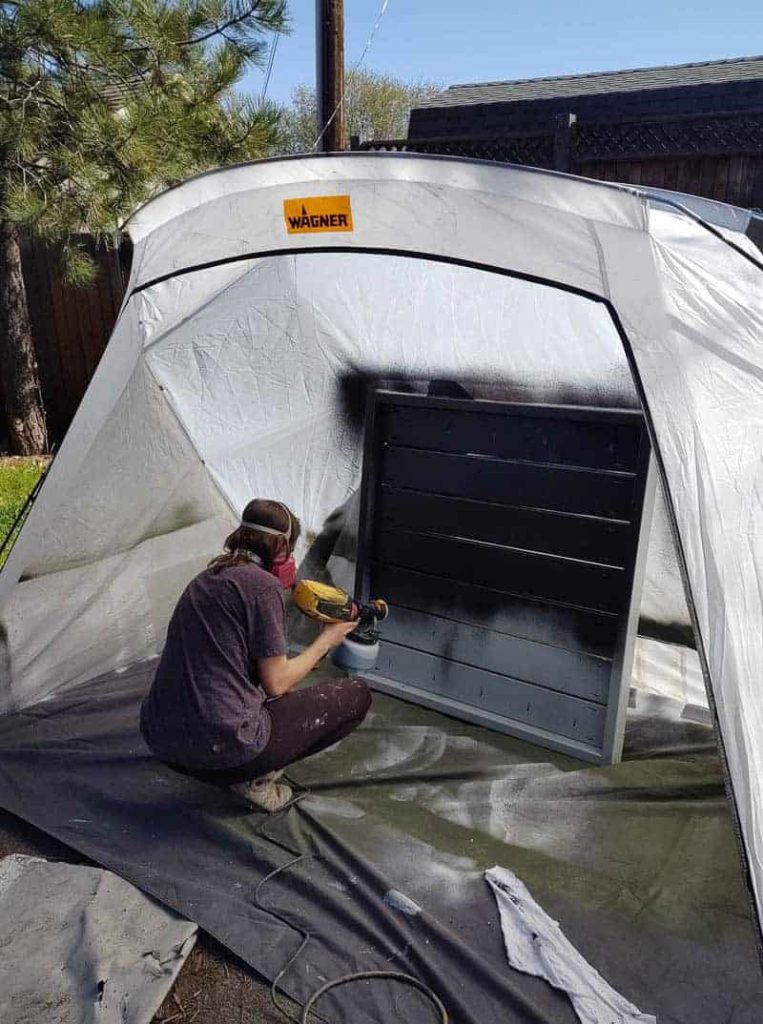 shows a woman using a Wagner paint tent and paint sprayer to paint a wood plant wall black outdoors