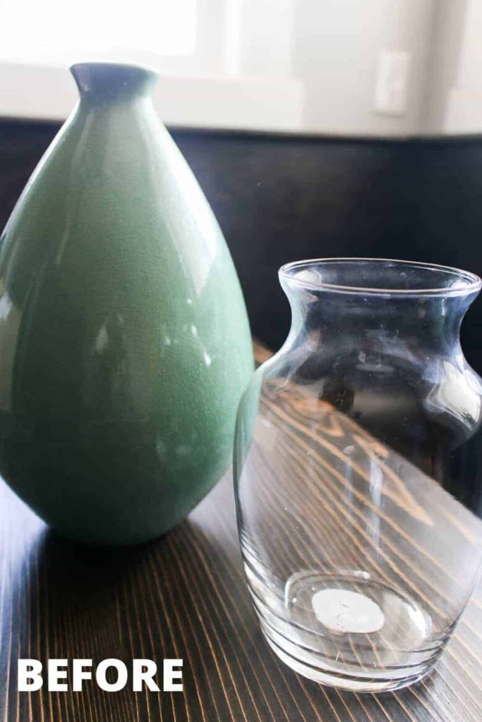 Two vases sit on a table. One vase is an ombre green ceramic vase, and the second is a shorter clear glass vase. Learn how to upcycle these thrifted vases into classic DIY vintage pottery.