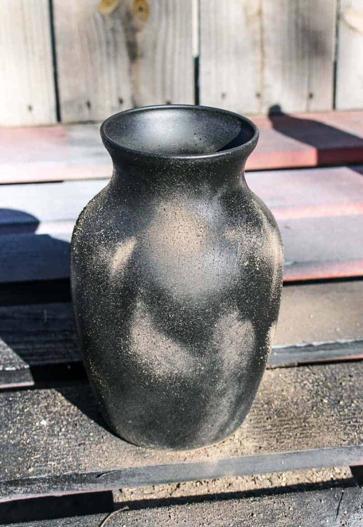 Creating a DIY pottery look on this painted black vase by tossing dirt onto wet spray paint.