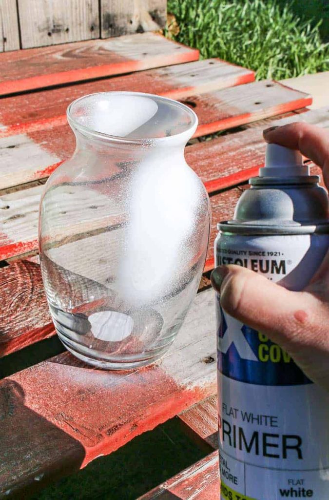 Spray painting a clear glass vase with flat white primer spray paint.