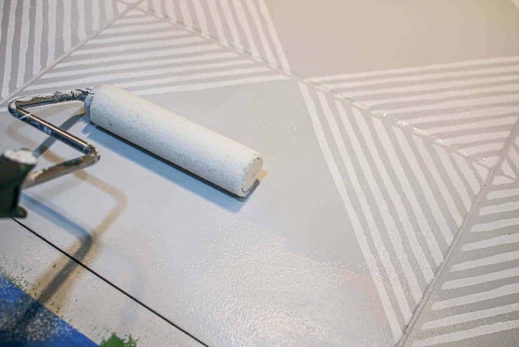 Using a large paint roller to touch up the base color of the painted tile floor. We used a neutral gray color with white stenciled geometric patterns