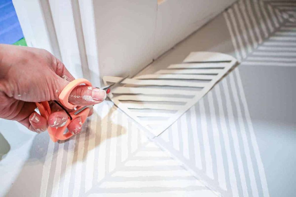 Carefully cutting geometric stencils to paint stripes on a bathroom floor as part of a stenciling floor tiles tutorial