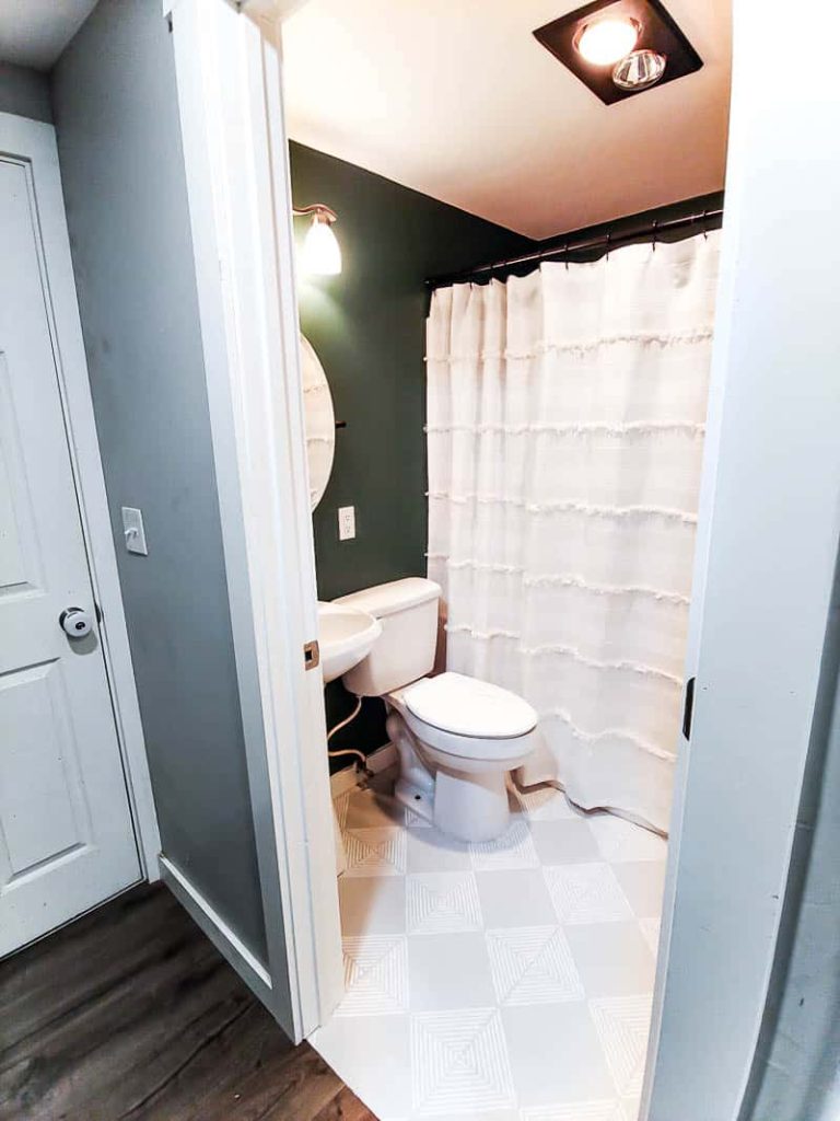 Our boho bathroom with teal walls and gray floors with white stripes and white shower curtain, sink, and toliet