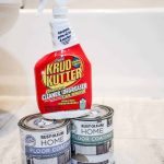 Shows two cans of Rust-Oleum home floor coating with Krud Kutrer spray bottle sitting on tan tile floor in a bathroom