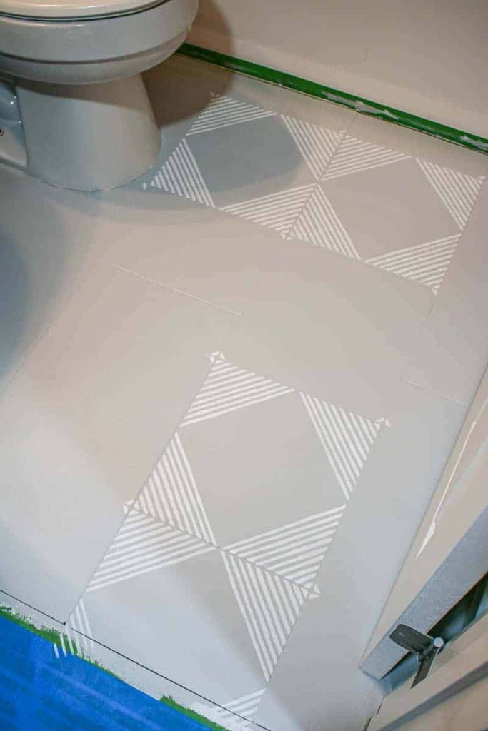 Painting geometric white and gray over a white stenciling floor tiles in our guest bathroom
