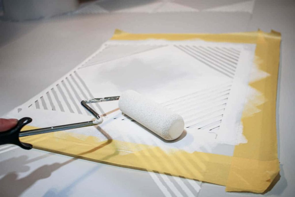 Using a geometric stencil for stenciling floor tiles to apply a neutral gray tile paint to our bathroom tile floor.