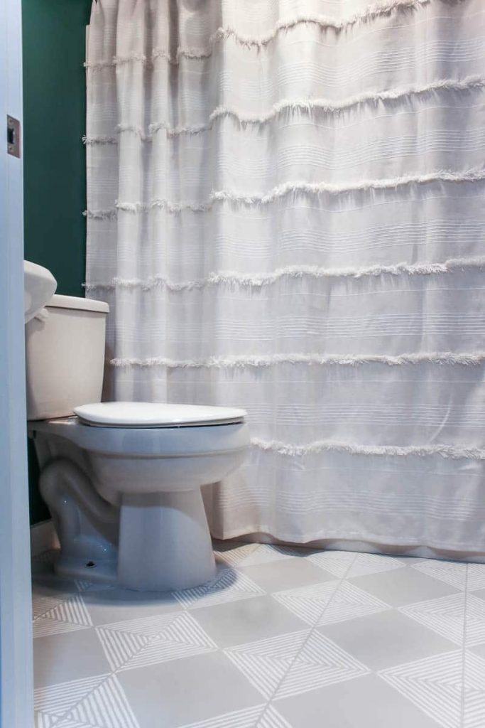 a boho style bathroom with bold teal walls, a white shower curtain, and painted tile floors with gray and white stripes