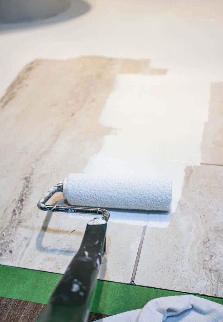 applying a base coat of white tile paint to tile floors using a paint roller. the base coat is important when stenciling floor tiles