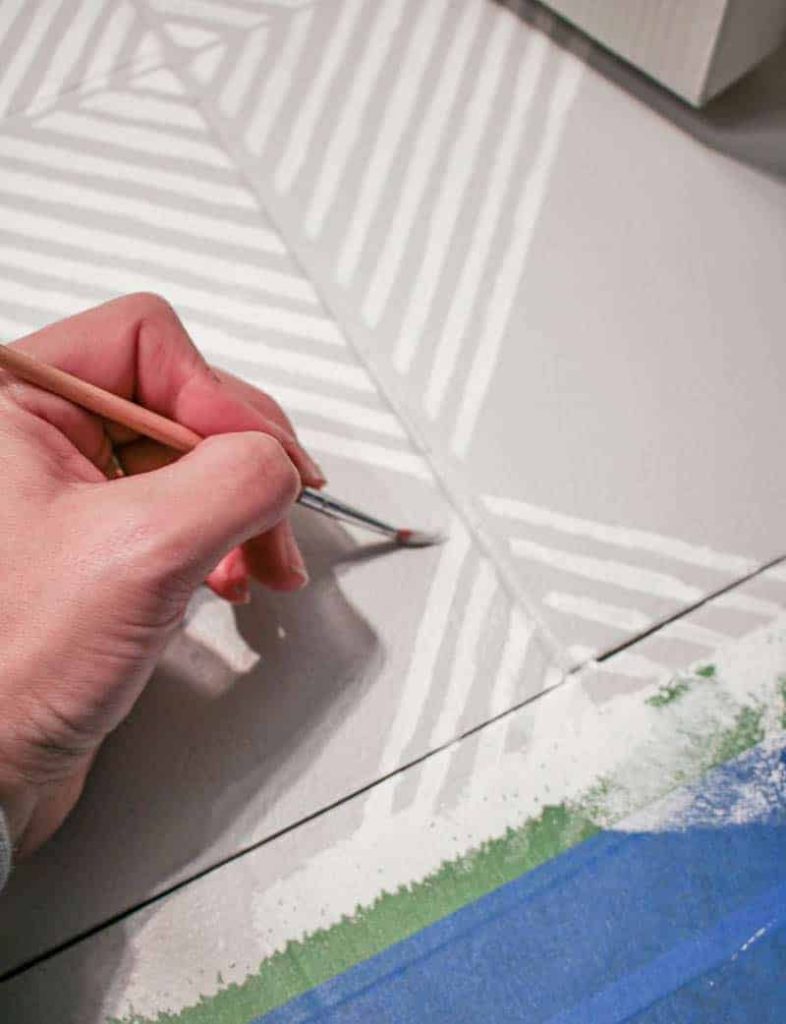 Use a small detail paint brush to touch up the stenciling floor tiles by painting white stripes on a gray tile floor