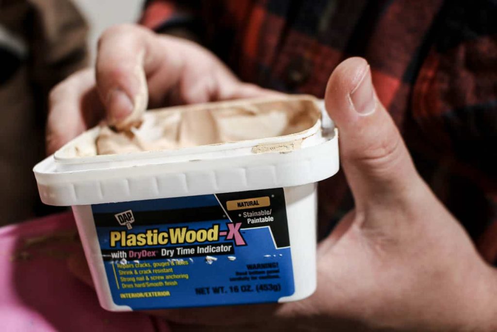 shows a finger wiping off some DAP Plastic Wood-x in the edge of the container