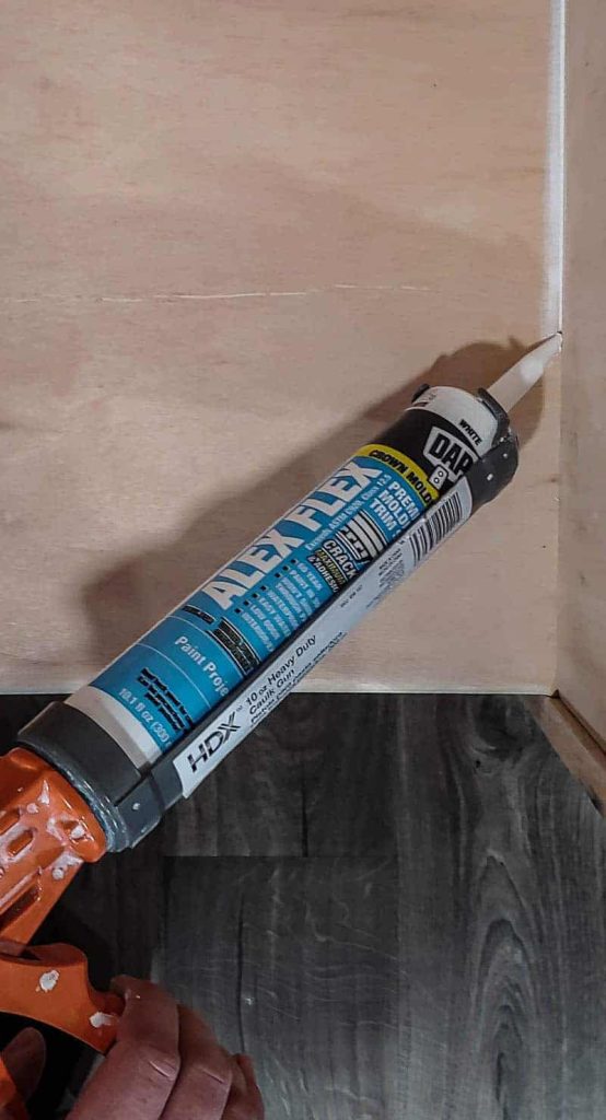 shows the brand DAP Alex Flex caulk being squeezed in between to panels of plywood