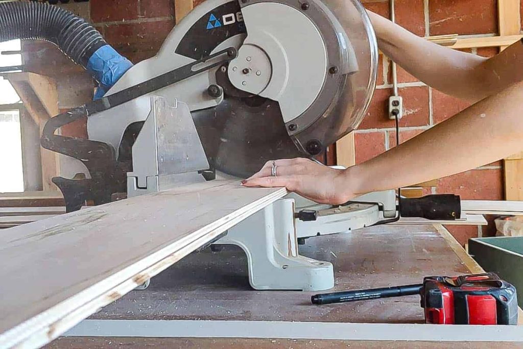 Using a miter saw to cut pieces of plywood down to size for the vertical shiplap wall.