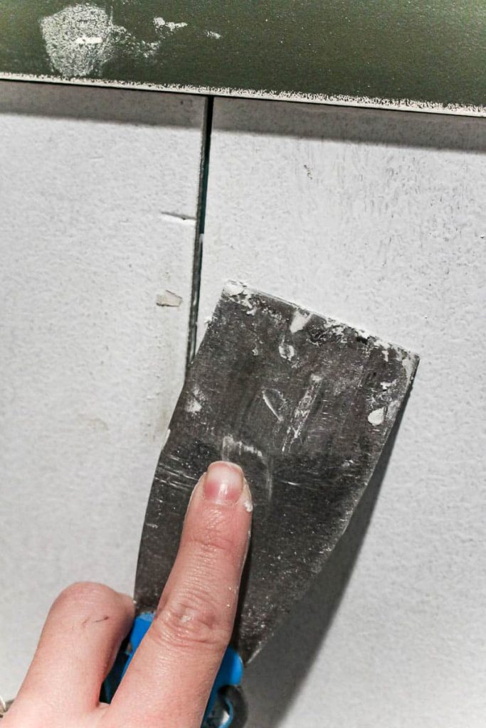 Filling nail holes in the vertical shiplap accent wall using a spackle scraper.