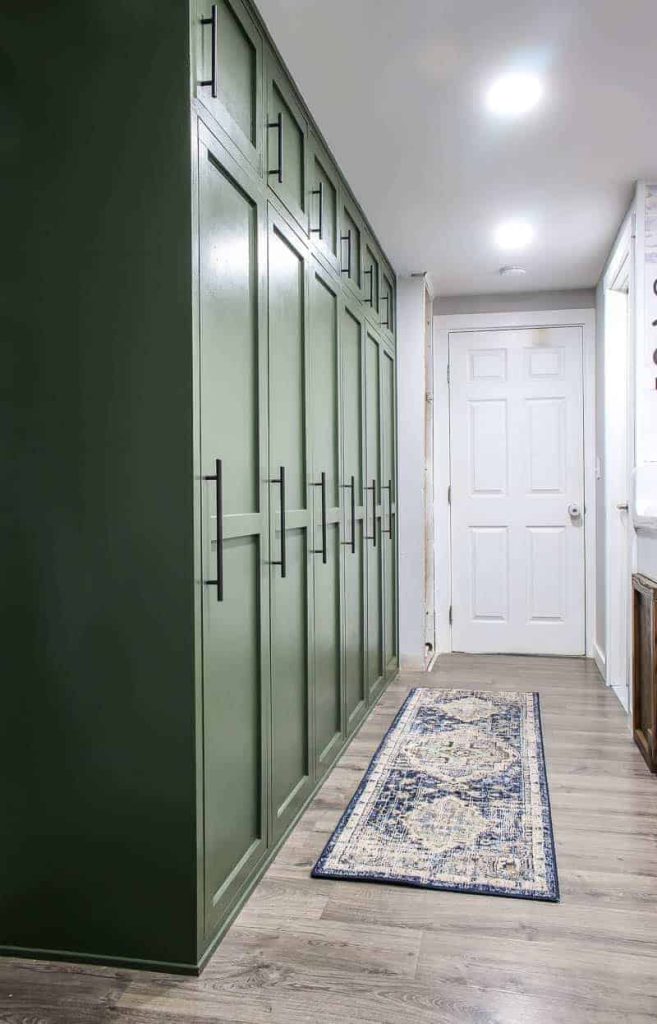 shows a farmhouse green mudroom lockers with blue and white boho runner rug on the gray wood floors in a white hallway and door