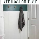 shows an angled view form the tub of the white vertical shiplap all with top half being dark teal and white door with gray floors with white stripes with overlay text that says how to make your own vertical shiplap