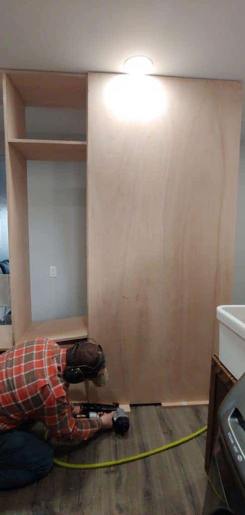 shows a man nailing the back of the mudroom lockers on