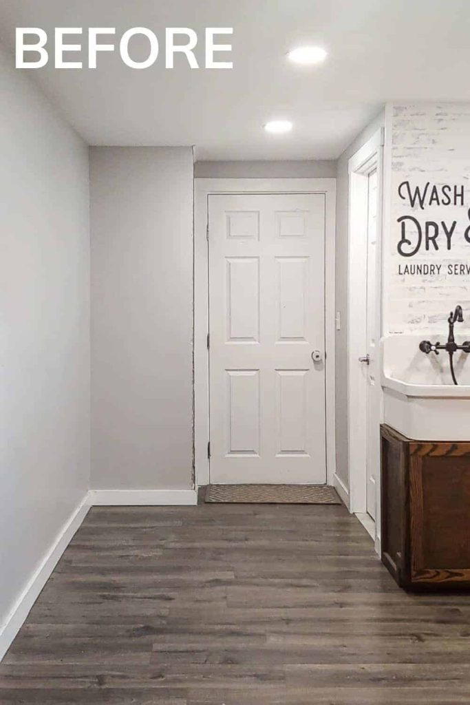 Shows the side of laundry room with white walls with Wash and Dry laundry service stencil and gray wood floors and farmhouse sink with text that says before