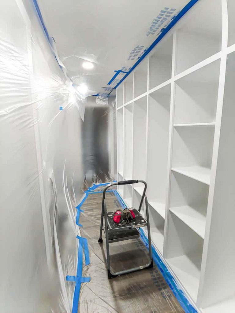 shows a hallway covered in plastic and tape with the mudroom painted white with primer and a step ladder 