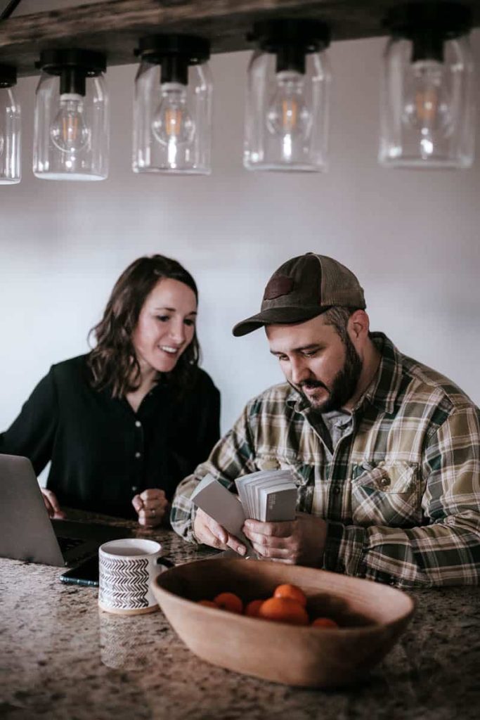 A man and a woman sit at a countertop in a kitchen, looking at paint swatches during their fixer upper home renovations.