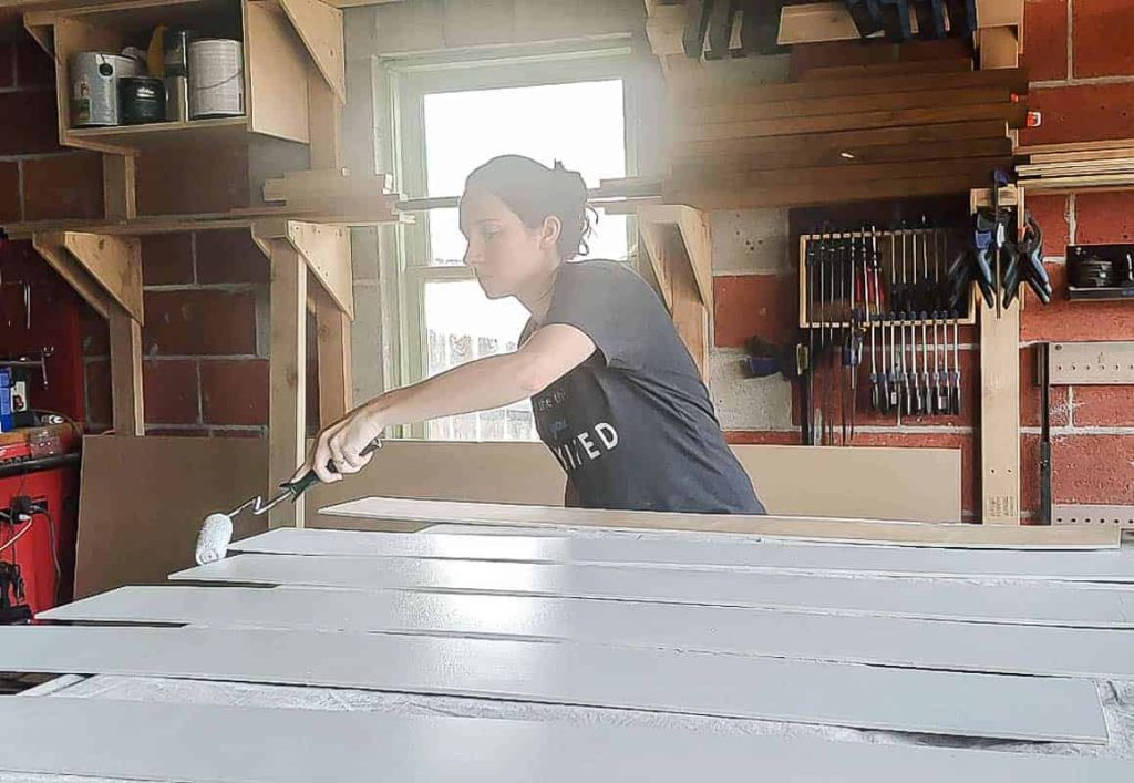 Chelsea uses a paint roller to paint the shiplap slats with white primer before installing in the bathroom.