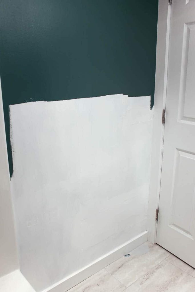 A bathroom wall, half painted white with primer and half painted teal. The lower white half if the bathroom wall will have a vertical shiplap wall.