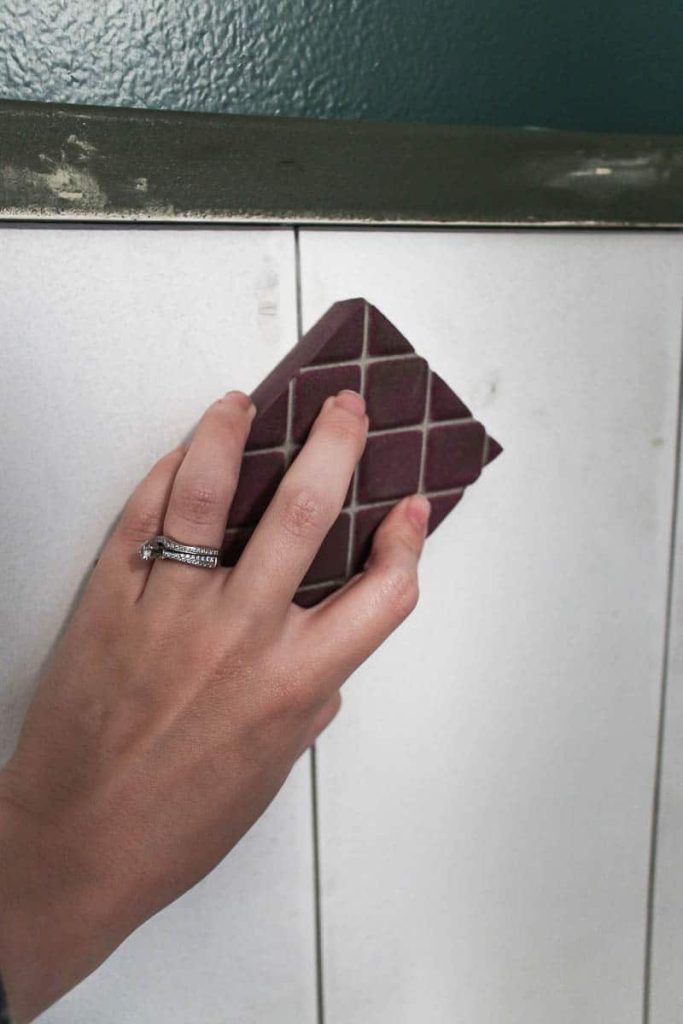 Using a sanding sponge to sand down the spackle-filled nail holes on the vertical shiplap wall.