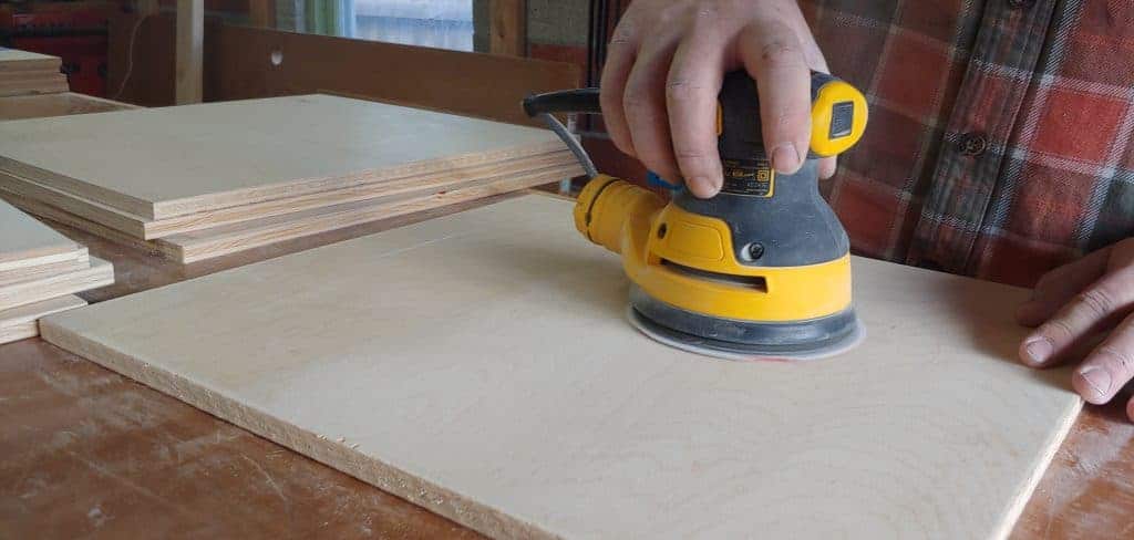 shows a hand using a sander to smooth out the square piece of plywood