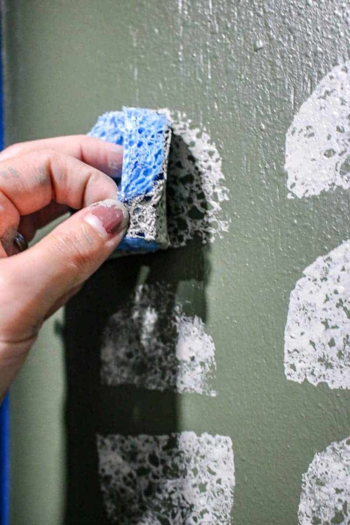 shows a hand using a sponge to paint white pattern the back of the mudroom lockers