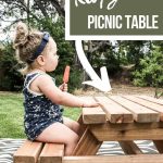 shows a side view of the toddler eating a Popsicle wearing a navy blue outfit on a wood picnic table on a boho black and white rug with overlay text that says how to build a kids picnic table and free plans