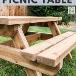 shows an angled view of the wood kids picnic table with a couple trees and grass in the background with overlay text that says kids picnic table, download free plans