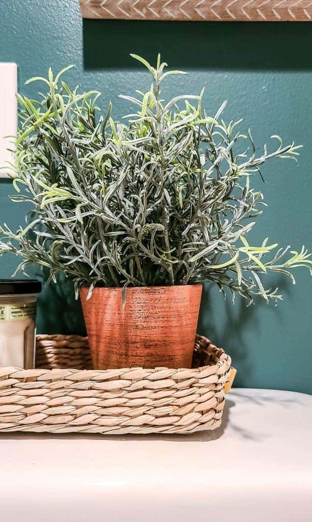 A potted plant and candle sit in a wicker basket on the back of a white toilet.