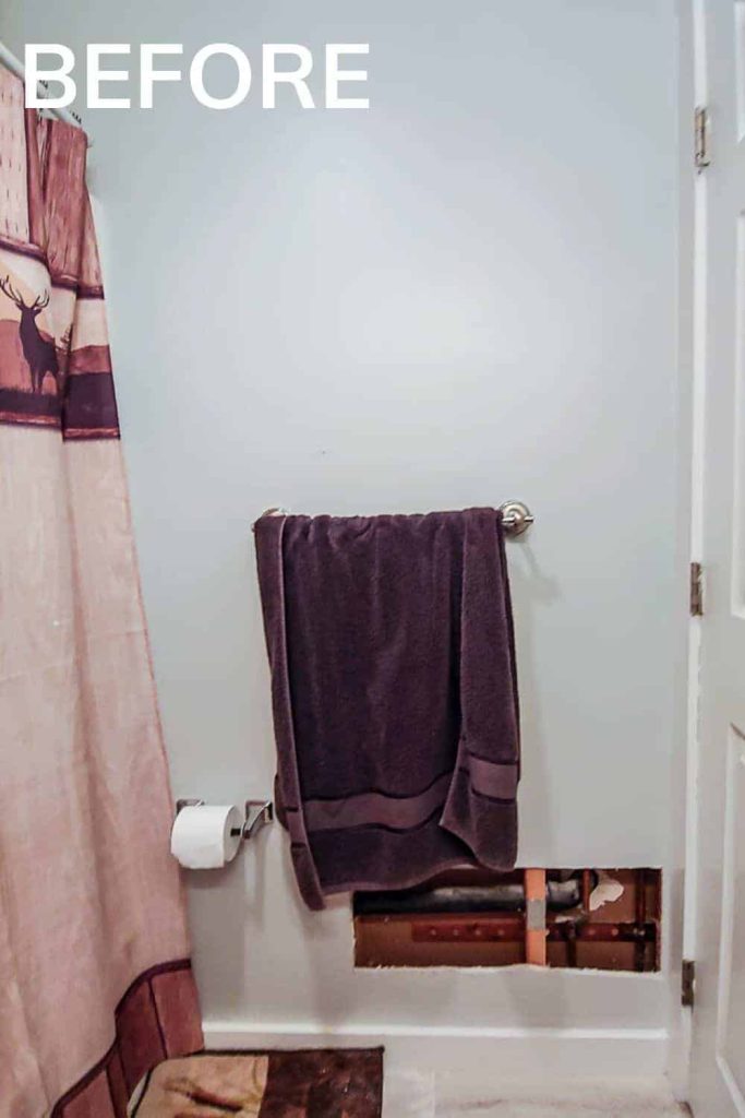 A look at the inside of our guest bathroom before our budget bathroom makeover - white walls, a towel holder, and a large hole in the lower right side of the dry wall