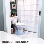 shows a corner of the bathroom with a toilet and white sink next to a white shower curtain with a dark teal wall and gray tile floors with white stripes with overlay text that says budget friendly small bathroom