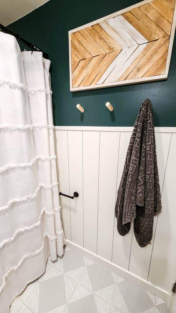 A small corner of our updated boho style bathroom, with a partial DIY white shiplap wall; the top half of the wall is painted deep green, and diy wooden wall art hangs in the middle of the wall.