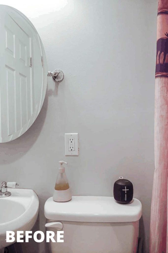 White bathroom walls, a vanity mirror, and a sliver of a white and red cabin themed shower curtain. 