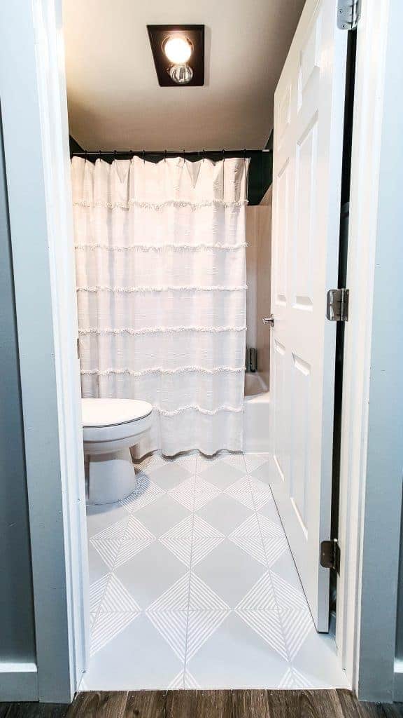 A look from the outside of our guest bathroom after our Buget Bathroom Makeover shows the newly painted grey and white tile floor and new white linen shower curtain.