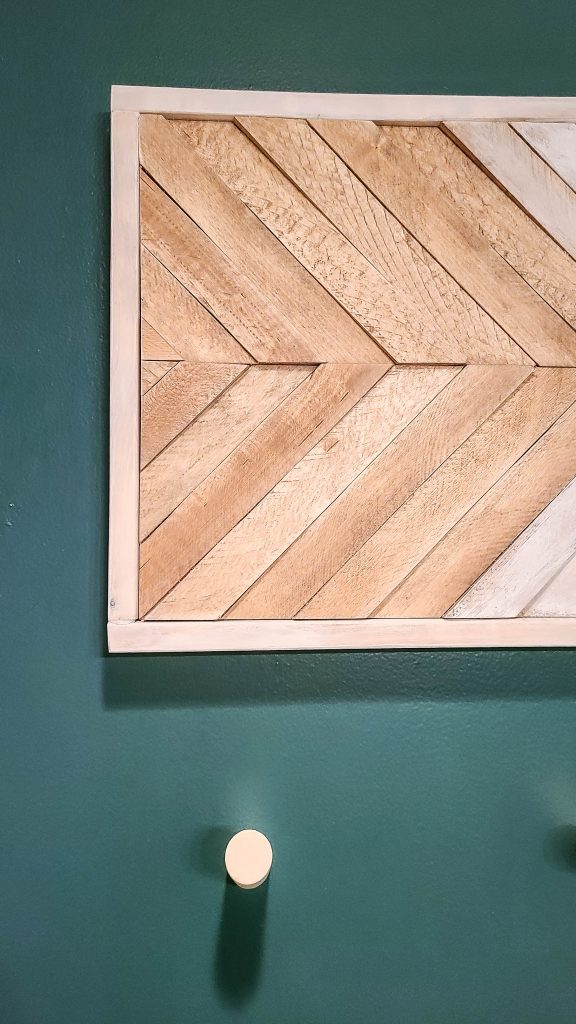 A portion of the DIY wood panel wall art shows raised wood panels, hanging against a deep green wall.