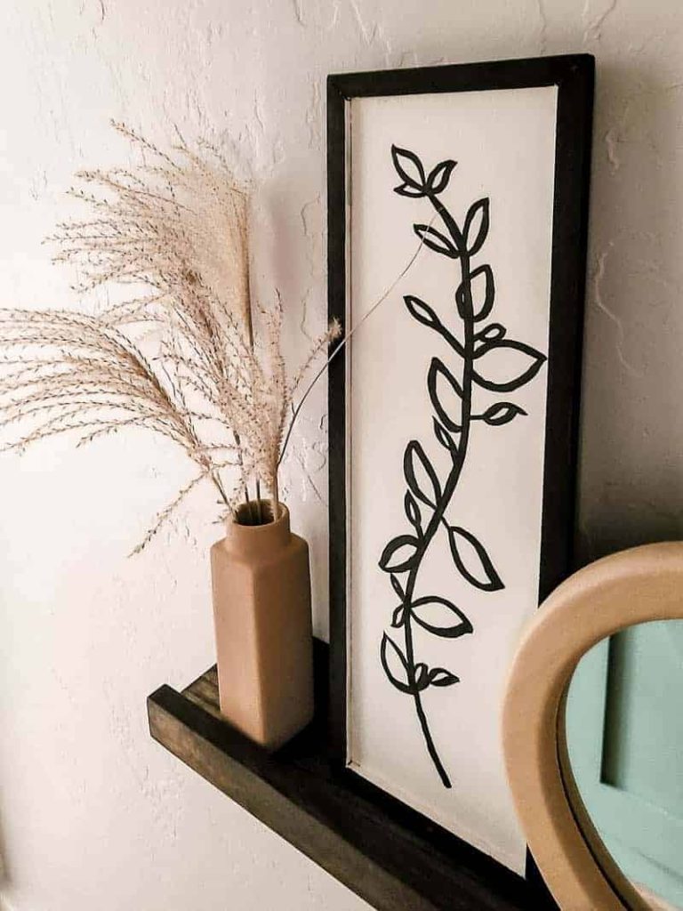 Newly painted tan boho vase with  stems of pampas grass on wood floating shelf with other bohemian style decor