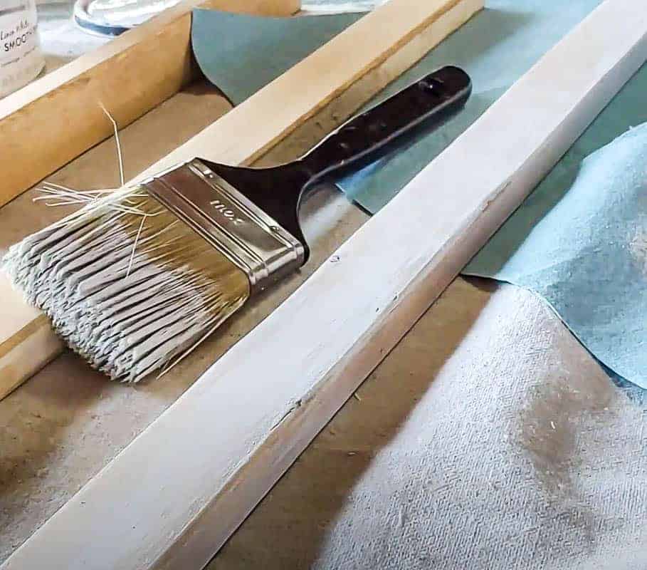 shows piece of 1x2 wood laying down on a drop cloth with a paint brush