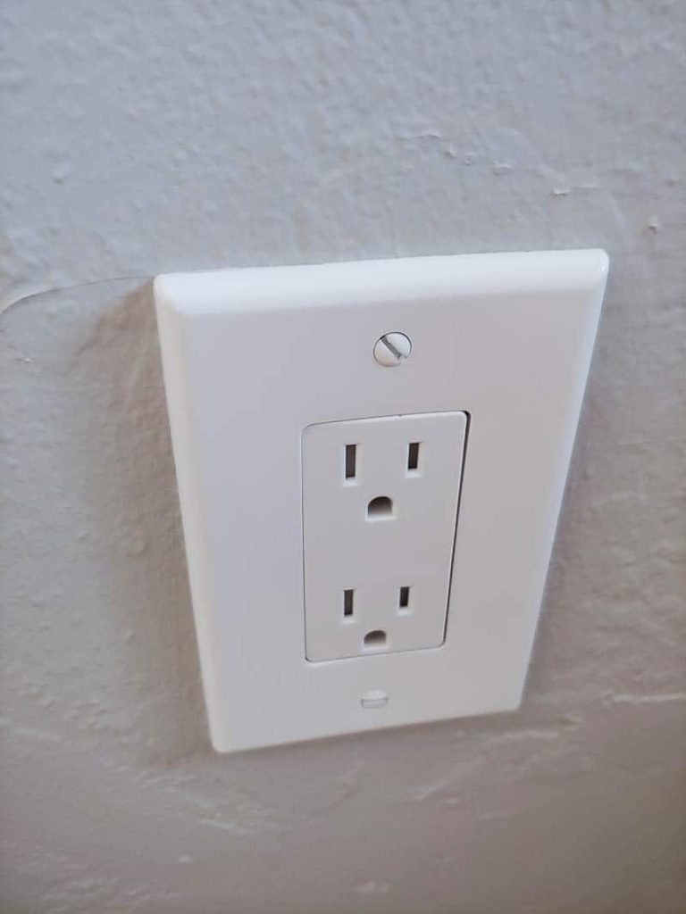A close up image of a brand new electrical outlet on a white wall, covered with a new white faceplate.