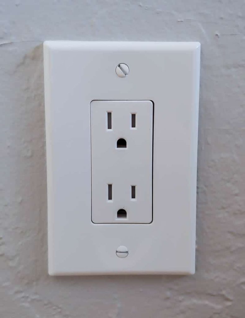 A close up image of a white electrical outlet and faceplate against a white painted wall.